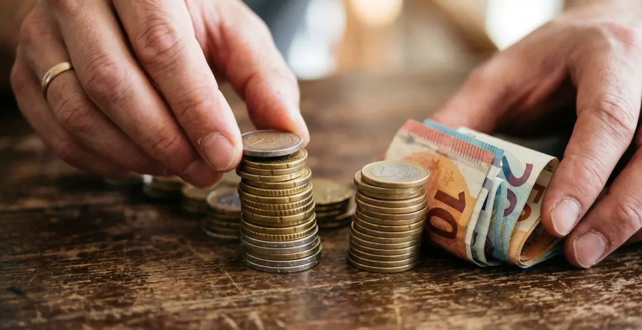 Gros plan sur des mains arrangeant des pièces et billets en piles organisées